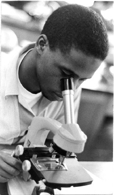 Student, either Roy Walker or Hubert Farbes, using a microscope.
